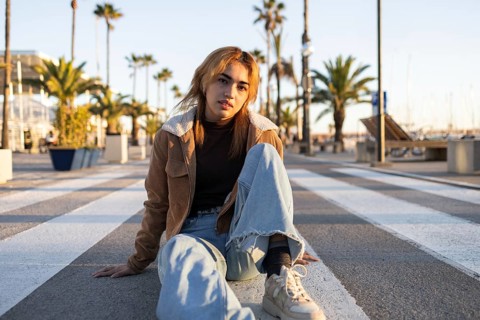 A casually dressed Mixed-race woman sits on a pedestrian crossing on a boardwalk, surrounded by