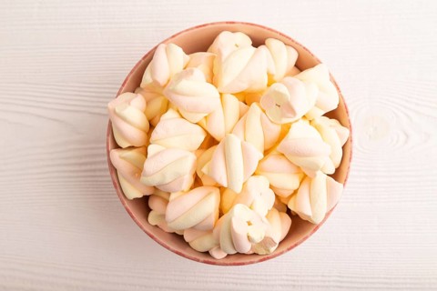 Orange and pink marshmallow in ceramic bowl on white wooden background, top view, flat lay, copy