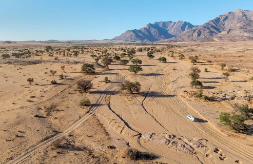 Aerial view of off-road car driving in dry riverbed and desert landscape on the Ugab River, behind
