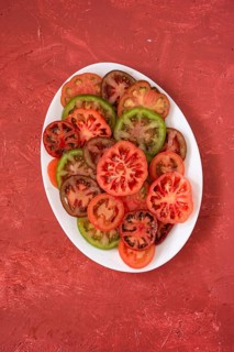 A variety of fresh heirloom tomatoes, sliced and arranged on a white plate, showcasing red, green,