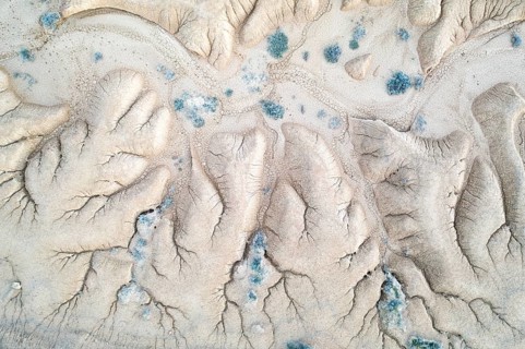 An aerial photograph captures striking erosion patterns in a barren landscape, displaying intricate