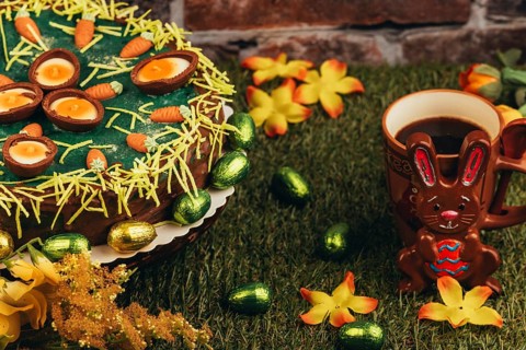 An Easter cake next to the Easter bunny, coffee cup and flower arrangement on grass