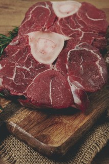 Knuckle on the bone, raw meat for ossobuco, on a wooden chopping board, with a sprig of rosemary,