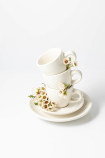 Stack of white ceramic cups and a saucer, elegantly garnished with fresh spring flowers on a white