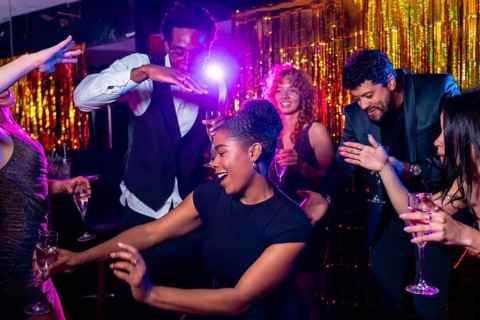 Cheerful multi ethnic friends dancing and drinking champagne, enjoying vibrant nightlife at