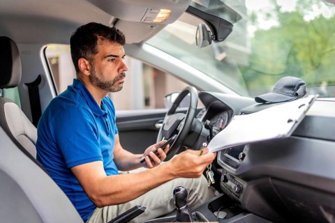 Delivery man using mobile phone and doing paperwork before deliver packages sitting inside a car