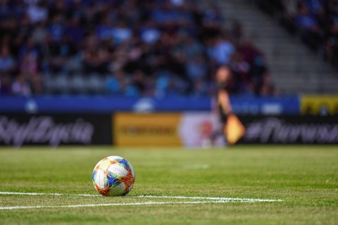 Ball on the soccer pitch with sideline referee and tribune in the background