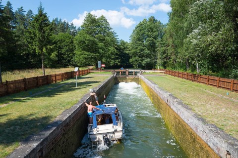 A boat navigates through the lock with green surroundings and blue sky in the background, Sluza