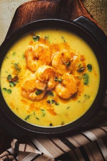 Creamy shrimp curry with spices, garnished with herbs, on a textured background, homemade, no