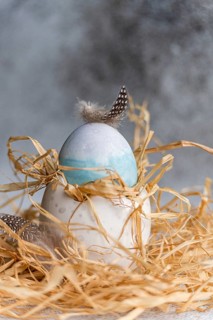 An Easter egg delicately decorated with a blue hue and adorned with natural feathers, nestled in a