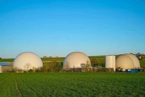Modern biogas plant with large dome structures surrounded by fields under a clear blue sky, Lower
