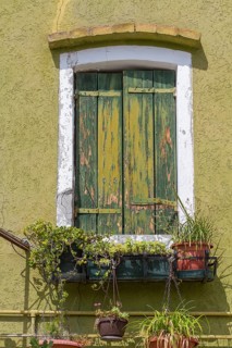 Old green window with weathered shutters and hanging plant pots under the Mediterranean sun,