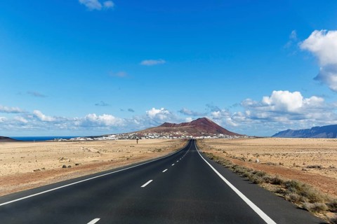 Empty straight country road and Soo village, Caldera Trasera on the horizon, El Jable, Lanzarote,