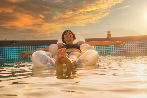 A young brunette Caucasian smiling enjoying the summer on a mat in the pool, at sunset in the
