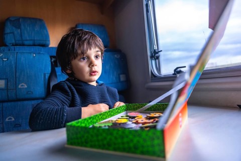 Young boy concentrating on completing a puzzle while sitting at a table inside a camper van, parked