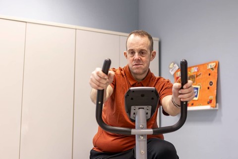 A man participates in a wellness activity on an exercise bike in a mental health day center,