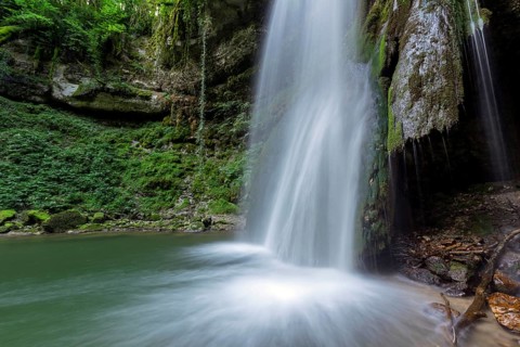 A waterfall flows into a small pool of water. The water is clear and the rocks are scattered around