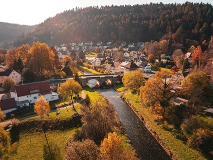 Picturesque autumnal village with river and bridge, surrounded by colourful trees and hills, Calw,