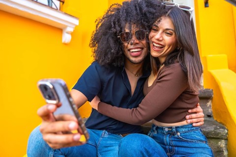 Young couple taking a selfie with a smartphone, hugging and smiling, sitting on colorful steps,