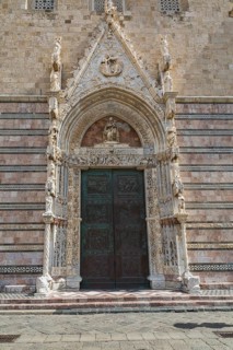 Ornate entrance door decorated with religious sculptures and figurines on facade at Messina