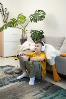 A young boy wearing headphones and a yellow shirt enjoys gaming on a console in a cozy living room,