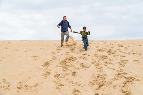 A joyful father and son run down the dune of Pilat, leaving footprints behind. Their laughter fills