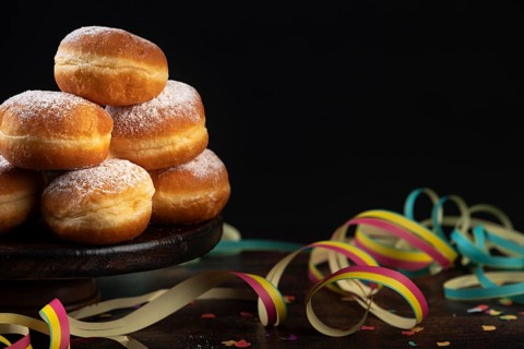 Pile of doughnuts with colourful paper streamers and confetti on a dark table, carnival