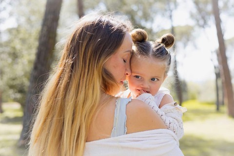 A pregnant woman holds her daughter lovingly outdoors, capturing a serene moment in nature. The