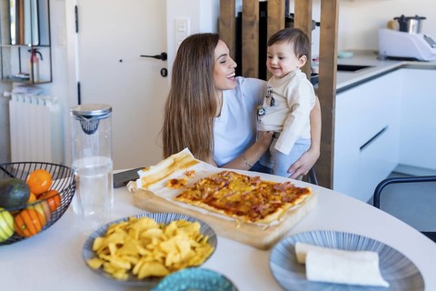 Mom holding her baby son, enjoying a delicious homemade pizza and tacos in their modern kitchen