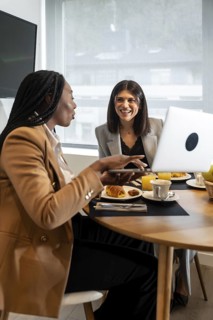 Two businesswomen enjoying breakfast and working on a laptop during their stay in a hotel room