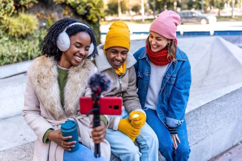 Group of cheerful young content creators filming a video blog outdoors in a winter city using a