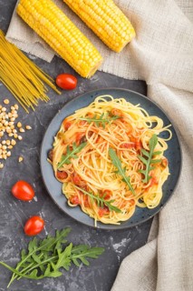 Corn noodles with tomato sauce and arugula on a black concrete background and linen textile. Top