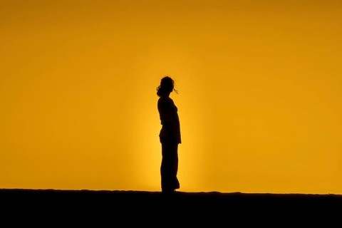 A woman's silhouette is silhouetted against a golden sunset on the sand dunes of Fuerteventura,
