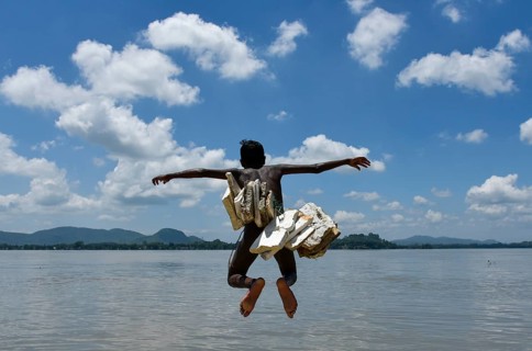A boy jump in the Brahmaputra river wearing polystyrene sheets to keep himself float in the water