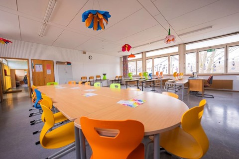 Classroom with long tables, colorful chairs and lampshades on the ceiling, homework supervision,
