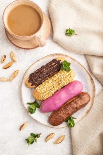 Set of eclair, traditional french dessert and cup of coffee on gray concrete background and linen