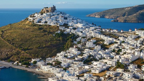 An ancient fortress towers over a coastal settlement of white houses on the edge of the sea,