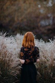 A woman with red hair stands among tall grasses in Quebec, Canada, embodying the serene beauty of