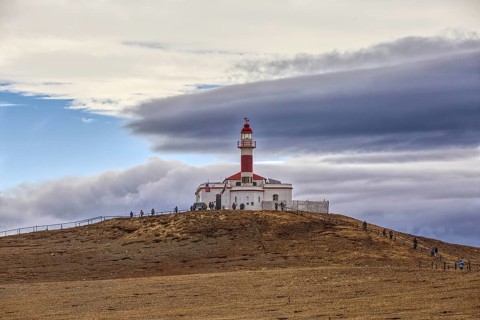 View of the lighthouse of Isla Magdelana and some tourists on a hill under a dramatically cloudy
