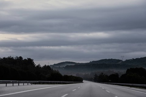An empty highway stretches into the distance under a dramatic sky filled with thick clouds. Fog