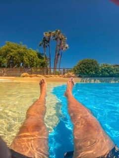 Legs of a tourist relaxing in a swimming pool with clear blue water at a water park, enjoying