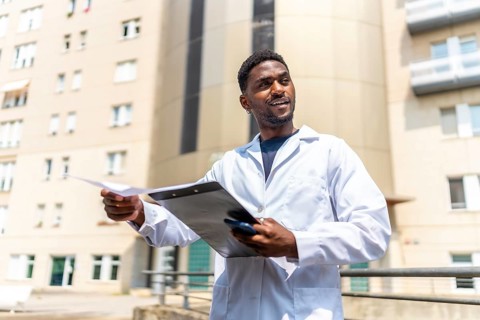 Confident African doctor with white lab coat working holding medical records outside the hospital