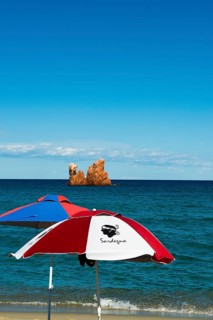 Sunshades on the beach and red rocks, Spiaggia di Cea, Tortoli, Sardinia, Italy