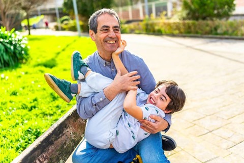 Grandfather and grandson are enjoying a playful moment together in a park, laughing and bonding on