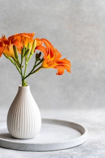 Vibrant orange Tiger Lily flowers arranged in an elegant white ceramic vase on a minimalist grey