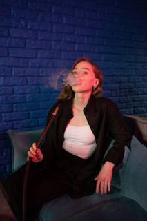 A relaxed young woman in a stylish outfit enjoys smoking hookah in a trendy lounge. She exhales