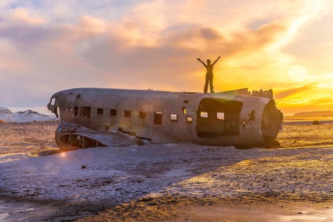 Woman on her back with her arms up on top of the Solheimasandur plane at a winter sunrise in