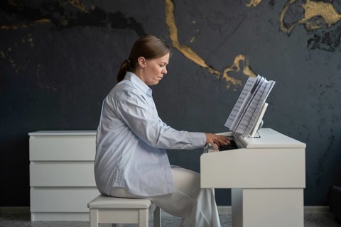 Woman dressed in white plays the piano in a stylish room with dark, textured walls and gold accents