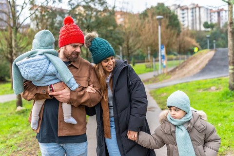 Smiling parents holding their children's hands, enjoying a leisurely stroll through a park on a