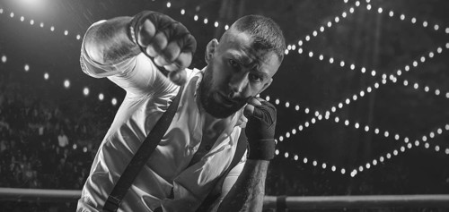 Black and white image of a bearded man in a white shirt and suspenders in the ring. The concept of